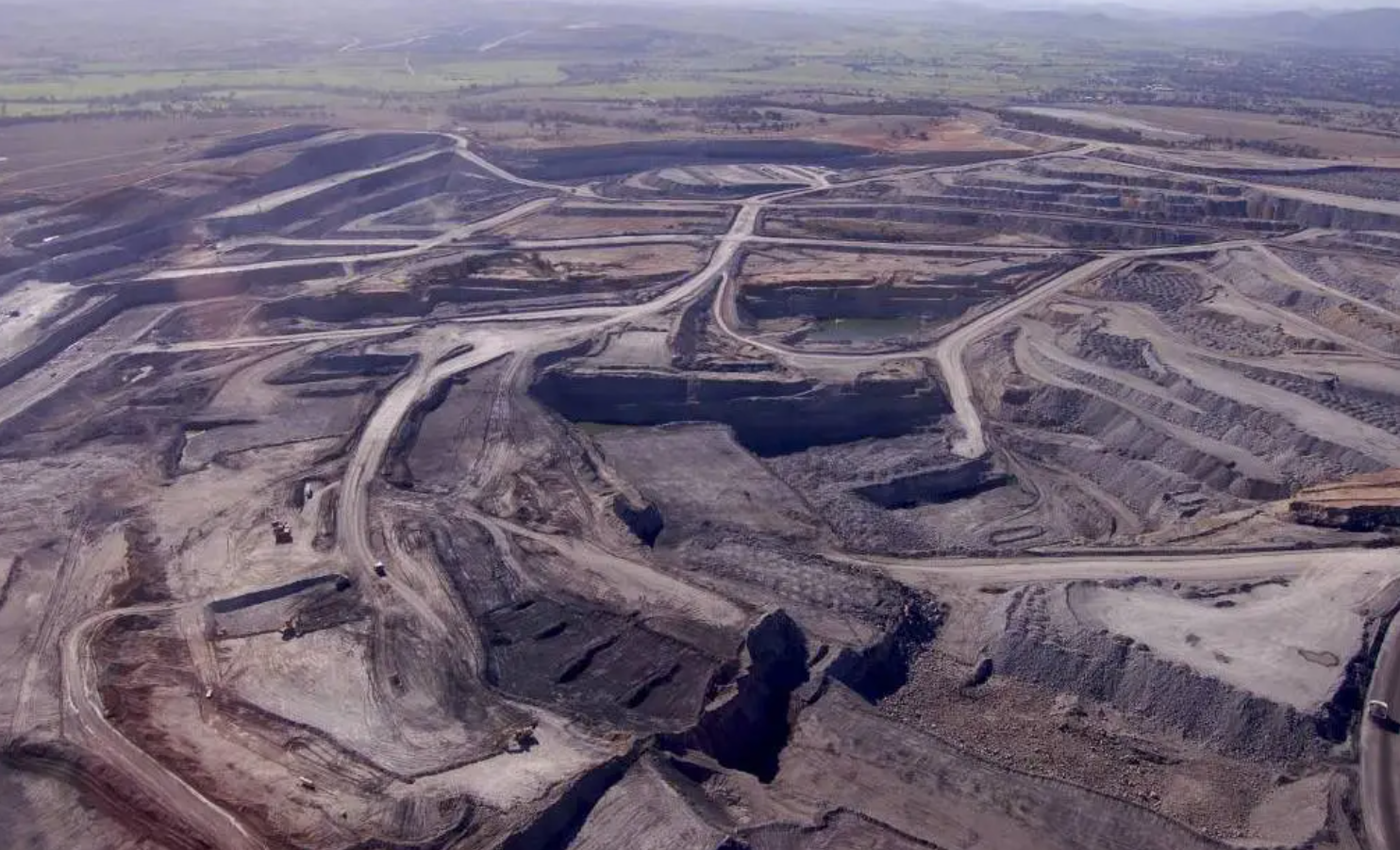 Aerial view of a large open-pit mine with terraced benches, haul roads and excavation areas extending across a wide landscape