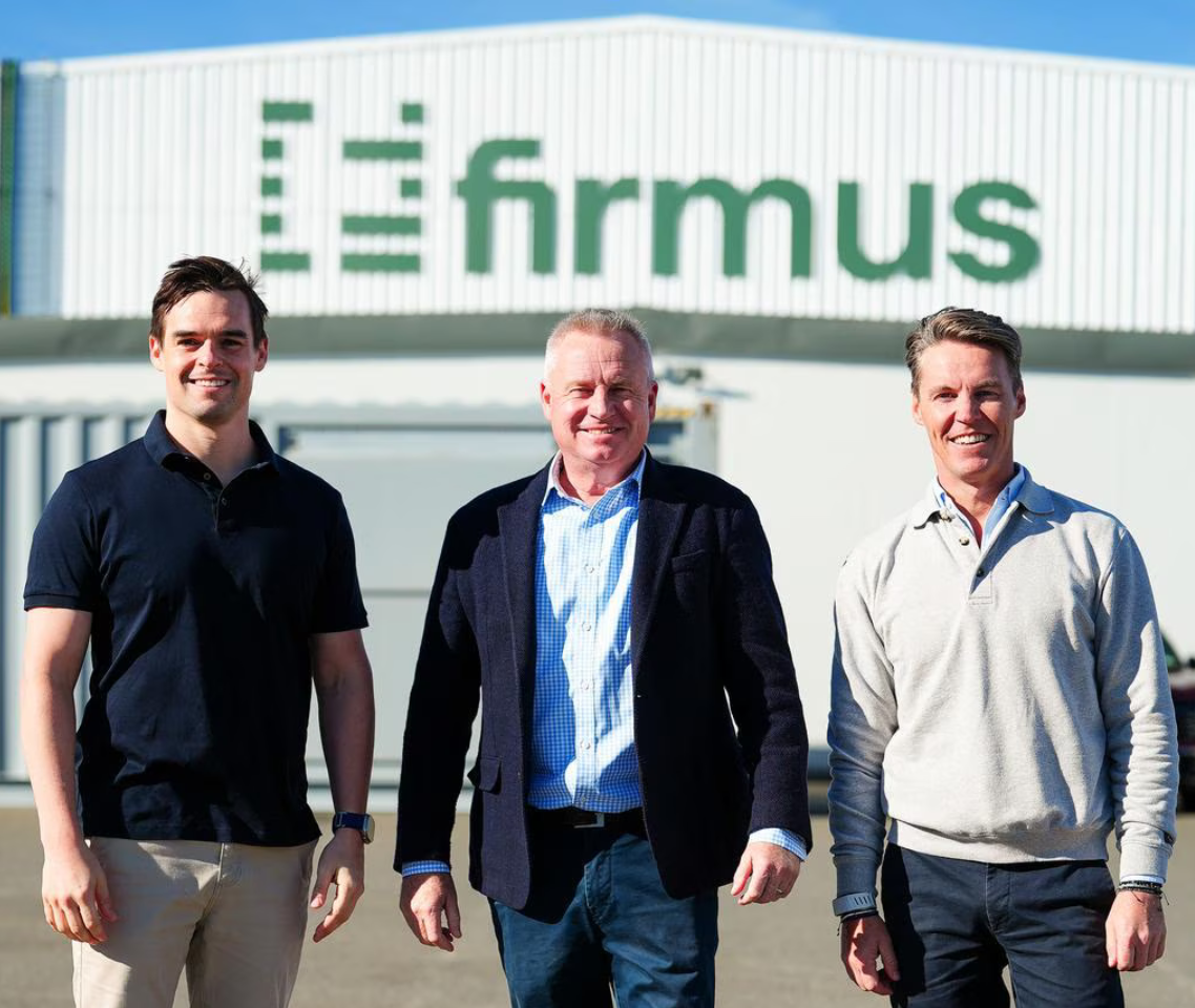 Three men standing outdoors in front of a warehouse with “Efremus” signage, smiling and facing the camera in business-casual clothing.