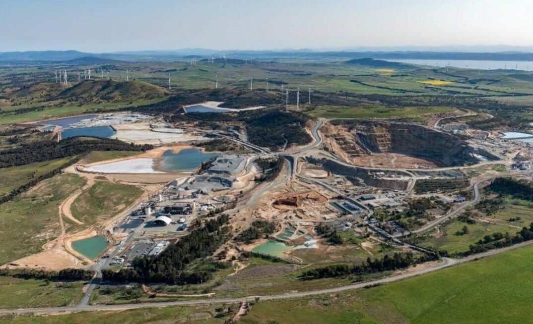 Aerial view of open pit mine with processing plant, tailings ponds, roads, and surrounding farmland and wind turbines