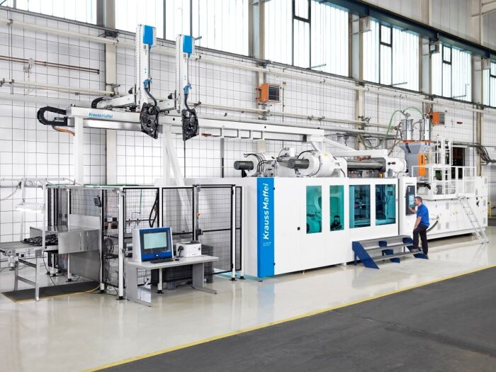 Large industrial manufacturing machine inside a clean factory, with automated robotic arms and operator control station.