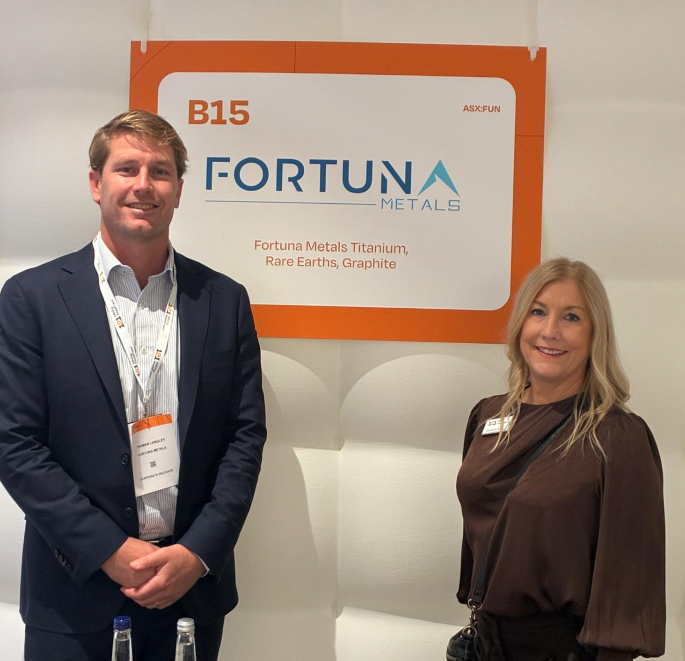 Two people standing beside a Fortuna Metals conference display promoting titanium, rare earths and graphite projects.