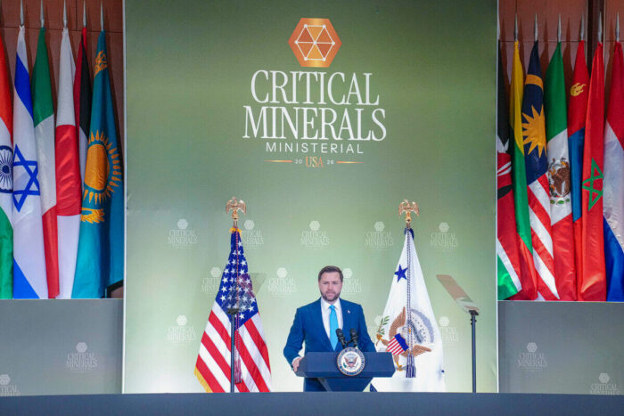 Speaker at podium beneath “Critical Minerals Ministerial USA 2026” backdrop flanked by US and international flags