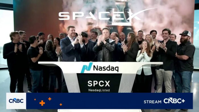 Crowd celebrates at a Nasdaq listing ceremony beneath a SpaceX backdrop, with SPCX ticker displayed on stage.