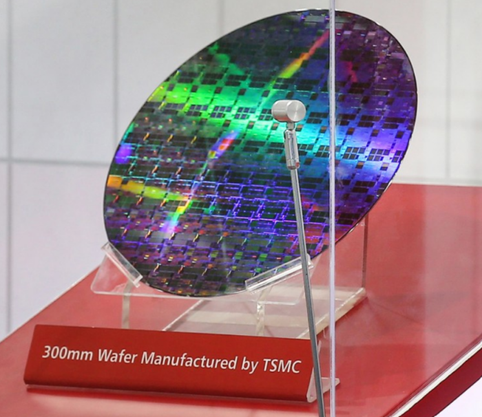 300mm semiconductor wafer manufactured by TSMC, displaying iridescent chip patterns across the silicon surface.