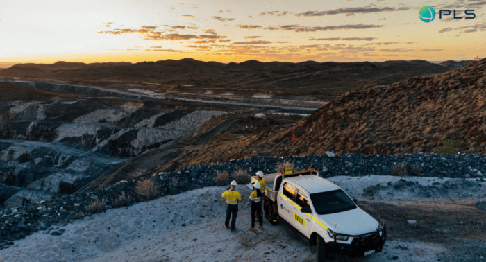 Aerial view of an open-pit mining operation at sunset, with workers and a utility vehicle overlooking the mine.