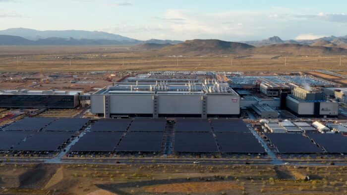 Aerial view of TSMC's semiconductor manufacturing complex, featuring large fabrication buildings and extensive solar arrays in a desert setting.