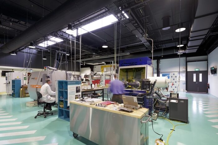Technicians work inside an advanced manufacturing laboratory filled with industrial machines, computers and testing equipment.