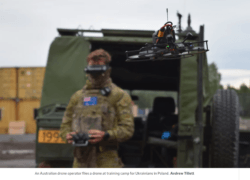 Australian soldier pilots a small FPV drone during military training in Poland, standing beside a camouflage support vehicle.