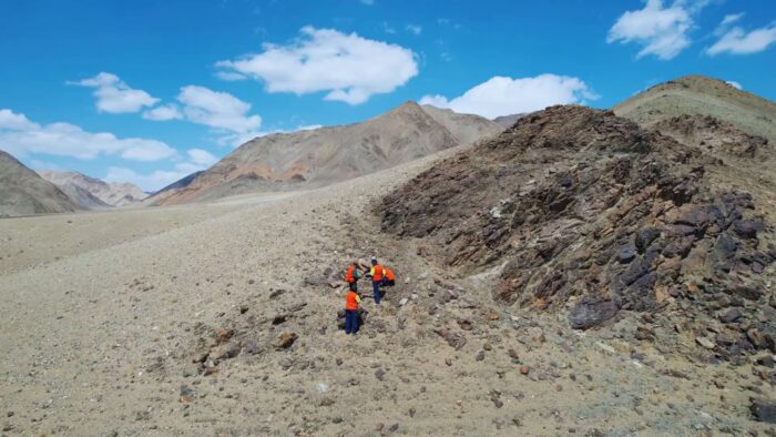 Field geologists in high-vis clothing examine rocky outcrops in a remote mountainous area of southwestern Mongolia.