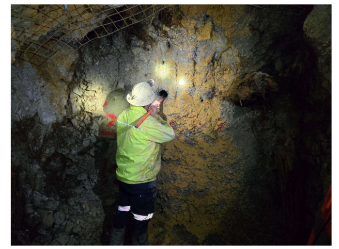 Underground worker inspecting an exposed rock face in a historic mine, illuminated by headlamps.