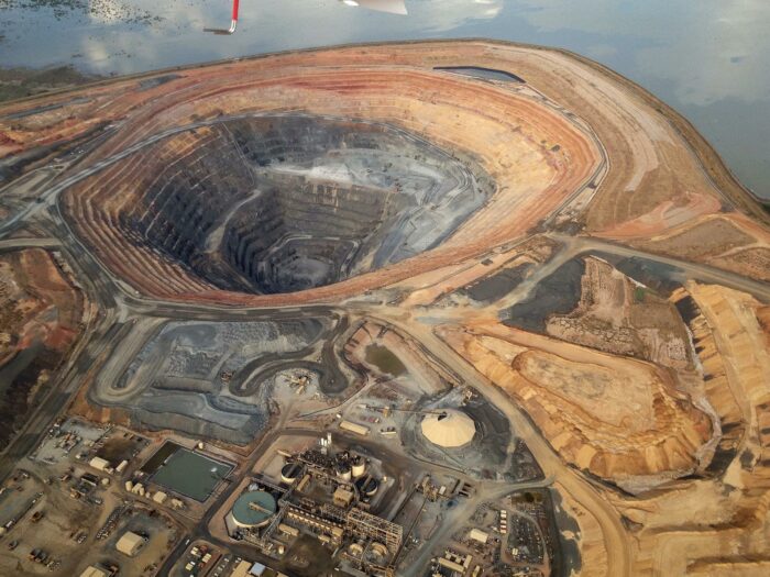Aerial view of a large open-pit mine with terraced walls, haul roads and processing facilities.