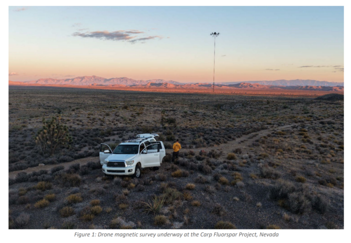 Drone conducting a magnetic survey above Nevada's Carp Fluorspar Project, with a field worker and vehicle below at sunset.