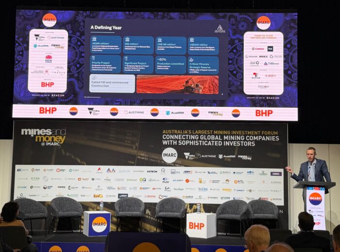 A speaker presents Arafura Rare Earths’ investment and project milestones at the IMARC mining conference, with sponsors displayed.
